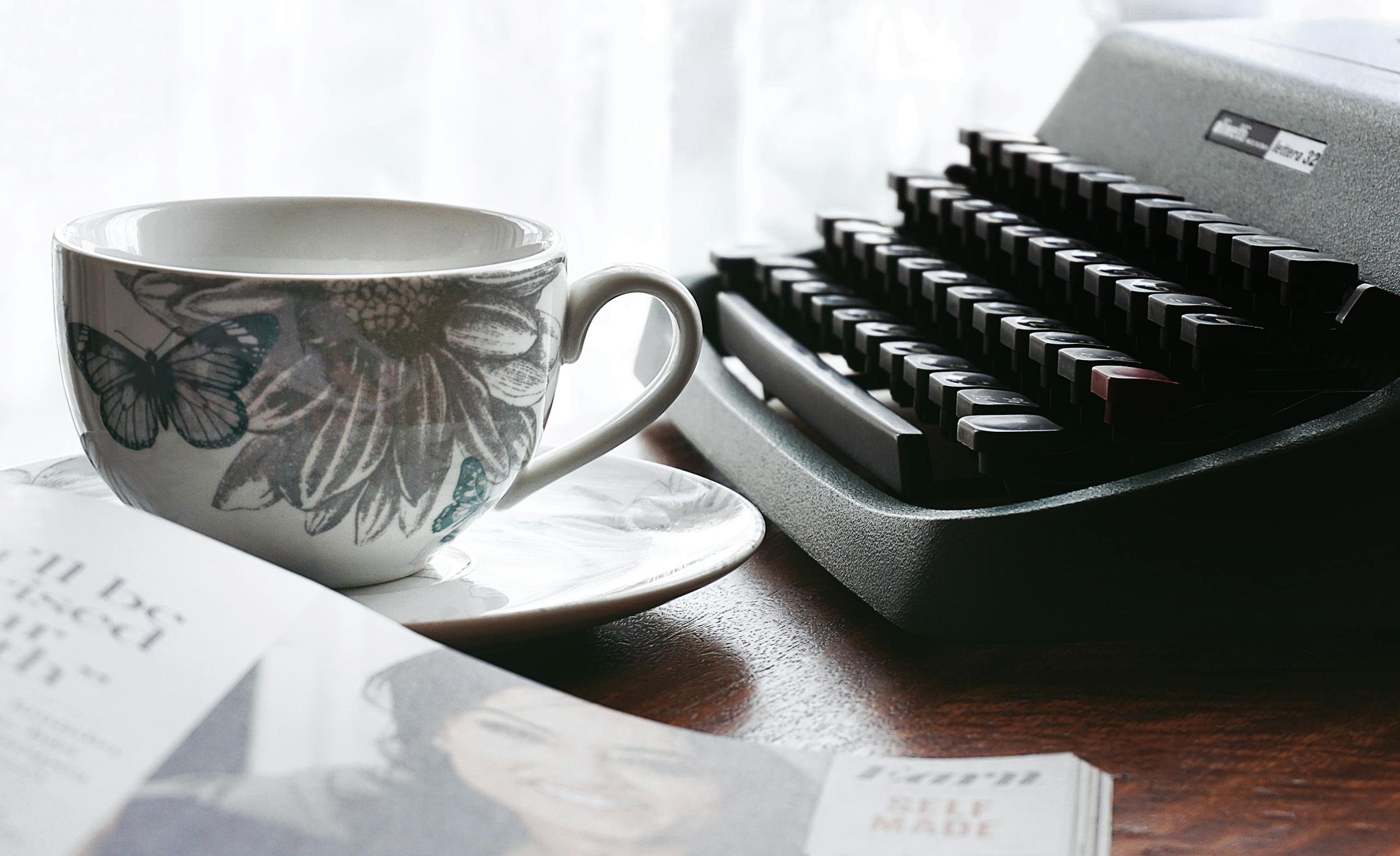 White and Gray Floral Ceramic Cup and Saucer Near Black Typewriter and Book